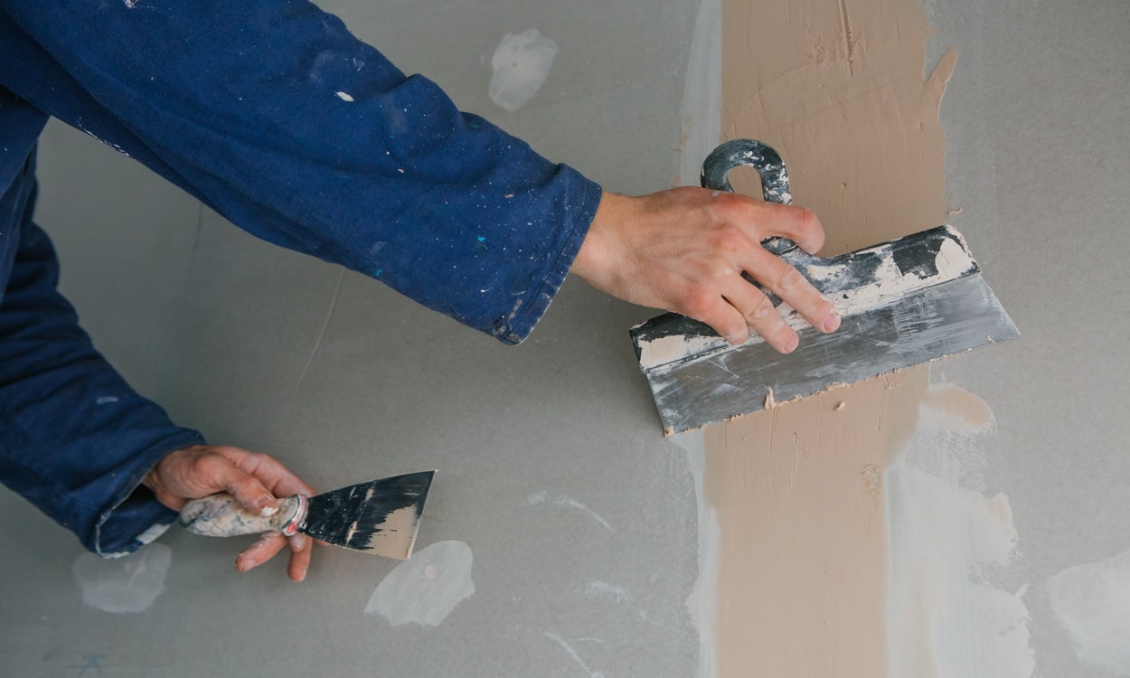 plasterer man works plastering two trowels plasterboard blue uniform min
